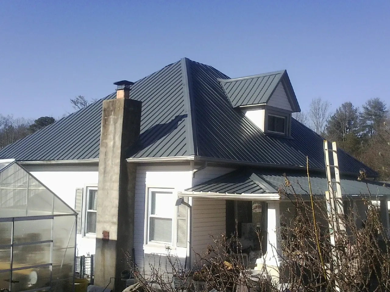 Dark blue standing seam metal roof on a white farmhouse with dormer — Slate & Tile Roof Repair by Roofing Brothers in Summerton