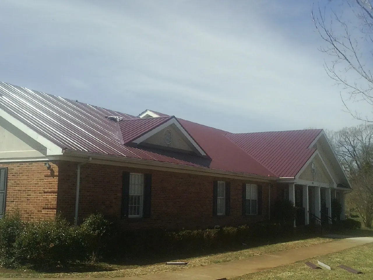 Red metal roof with gabled entries on a long brick building, from a Hail Damage Roof Repair job in Summerton