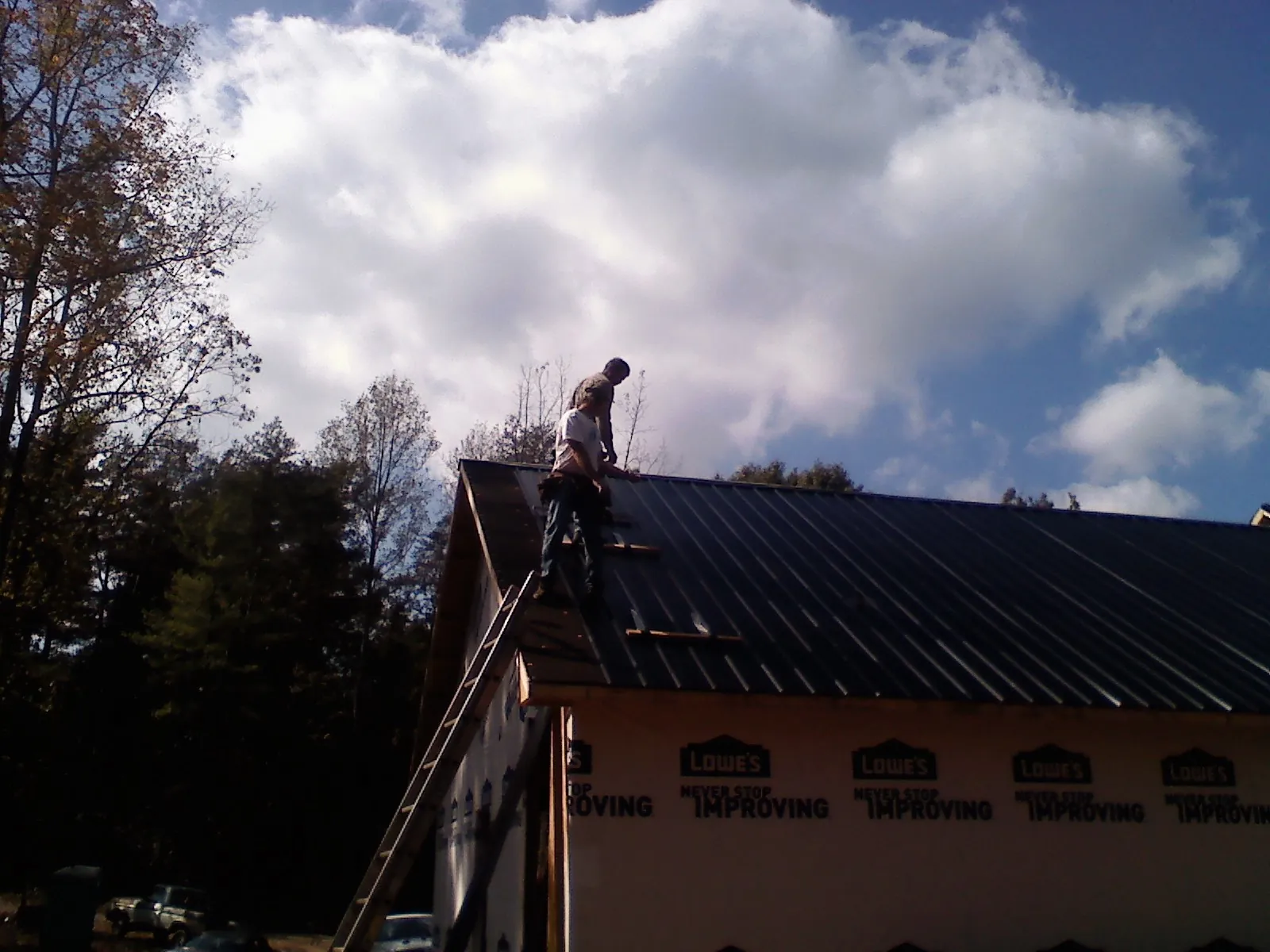 Roofer fastening dark metal panels high against a cloudy sky, from a Roof Inspection job in Summerton