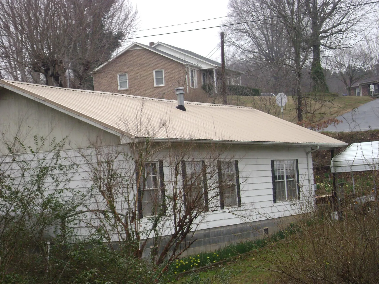 Tan metal roof on a white sided house set into a hillside — Commercial Roofing by Roofing Brothers in Summerton